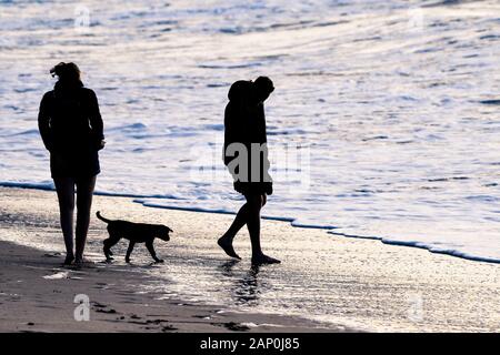 Die Silhouette von Menschen ihren Welpen nehmen für einen abendlichen Spaziergang auf den Fistral Beach in Newquay in Cornwall. Stockfoto