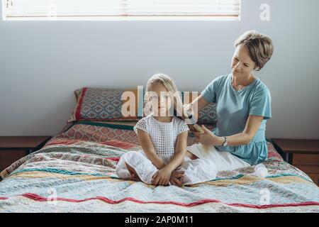 Mutter tun Haar Zopf zu ihrer Tochter auf dem Bett Stockfoto