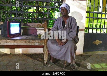 Typische Straße oder Gehweg Szene in der ägyptischen Hauptstadt Kairo: eine bawaab sitzt auf dem Nil Insel Zamalek neben einem laufenden Fernseher vor dem Eingang eines Hauses und wachen auf 10/14/2019. Die Funktion des Bewaab ist vielschichtig: auf der einen Seite steuert, wer das Gebäude betritt, Auf der anderen Seite er, seine Familie oder seine Helfer für die Bewohner für kleinere Dienste wie Botengänge oder einfache Reparaturen gegen eine geringe Gebühr zur Verfügung stehen. Foto: Matthias Toedt/dpa-Zentralbild/ZB/Picture Alliance | Verwendung weltweit Stockfoto