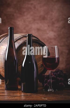 Glas Rotwein und zwei Flaschen mit Trauben und Holzfass im Hintergrund und kopieren Raum Stockfoto