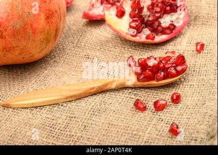 Reifer saftiger Granatapfel, Granatapfelsamen und Granatapfelsamen auf einem Holzlöffel auf dem Hintergrund rauer Homespun-Qualität. Nahaufnahme Stockfoto