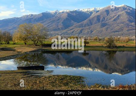 Blick auf Kerkini See im Norden Griechenlands ist mit traditionellen Holzmöbeln Fischerboot und Teil des schneebedeckten Mount Beles Stockfoto
