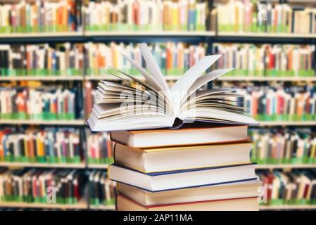 Geöffnete Buch auf einem Haufen vor einem großen Bücherregal | Verwendung weltweit Stockfoto