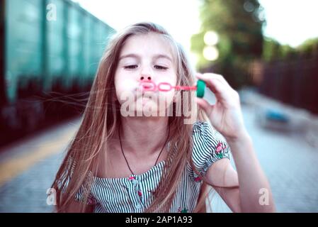 Porträt einer wunderschönen kleinen Mädchen bläst Seifenblasen. Ein Kind spielt mit Blasen, auf grünem Hintergrund. Im Freien Stockfoto