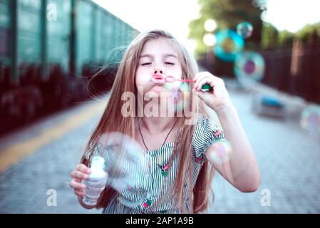 Porträt einer wunderschönen kleinen Mädchen bläst Seifenblasen. Ein Kind spielt mit Blasen, auf grünem Hintergrund. Im Freien Stockfoto