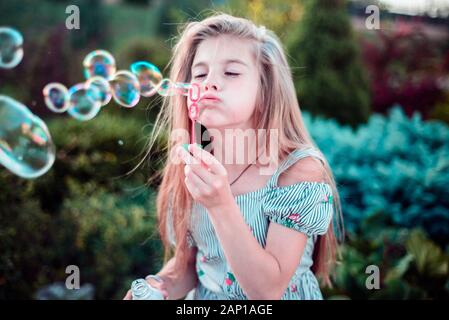 Porträt einer wunderschönen kleinen Mädchen bläst Seifenblasen. Ein Kind spielt mit Blasen, auf grünem Hintergrund. Im Freien Stockfoto