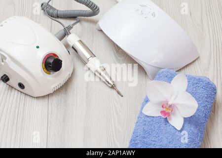 Fräser, LED-UV-Lampe und Handtuch mit weissen Orchideenblüte auf grau Holz- Hintergrund. Eine Reihe von kosmetischen Werkzeuge für professionelle Hardware Maniküre. Stockfoto