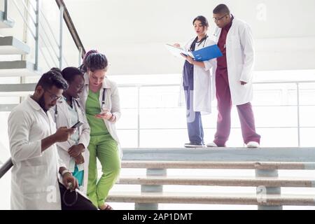 Junge Ärzte, gemischten Rennen, Sitzen, Stehen auf der Treppe, im Flur des Krankenhauses. Sie betrachten x-Strahlen, die Verwendung von Minianwendungen in der Medizin zu arbeiten. Peo Stockfoto