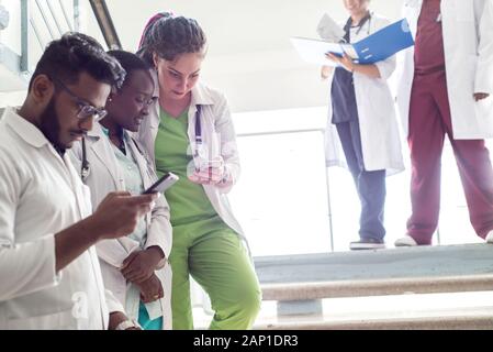 Junge Ärzte, gemischten Rennen, Sitzen, Stehen auf der Treppe, im Flur des Krankenhauses. Sie betrachten x-Strahlen, die Verwendung von Minianwendungen in der Medizin zu arbeiten. Peo Stockfoto