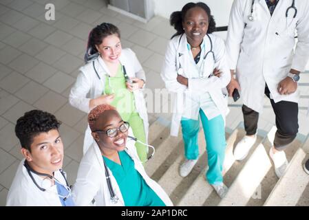 Junge Ärzte, gemischten Rennen, Sitzen, Stehen auf der Treppe, im Flur des Krankenhauses. Sie betrachten x-Strahlen, die Verwendung von Minianwendungen in der Medizin zu arbeiten. Peo Stockfoto