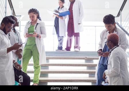 Junge Ärzte, gemischten Rennen, Sitzen, Stehen auf der Treppe, im Flur des Krankenhauses. Sie betrachten x-Strahlen, die Verwendung von Minianwendungen in der Medizin zu arbeiten. Peo Stockfoto