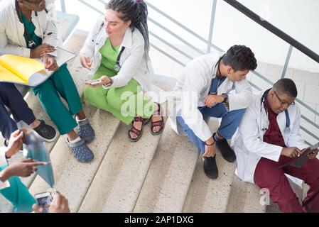 Junge Ärzte, gemischten Rennen, Sitzen, Stehen auf der Treppe, im Flur des Krankenhauses. Sie betrachten x-Strahlen, die Verwendung von Minianwendungen in der Medizin zu arbeiten. Peo Stockfoto