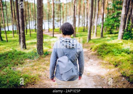 Frau mit einem kleinen Rucksack auf einen Spaziergang auf einem sandigen Weg in die blaubeere Wald im Sommer Stockfoto