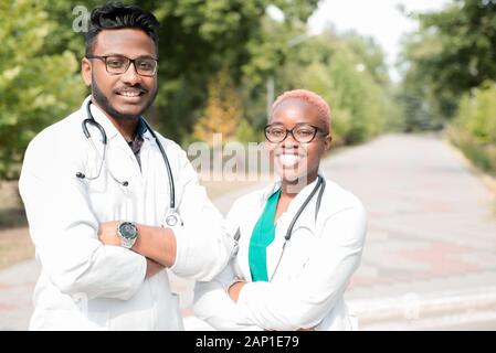 Porträt der jungen Ärzte. Indische Kerl, schwarze Mädchen. Menschen in weißen Kitteln, Gläser, mit stethoskope. Im Freien Stockfoto