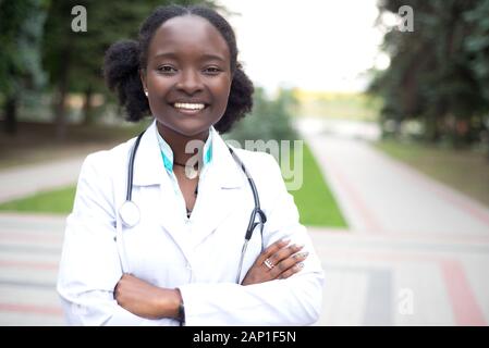 Portrait einer jungen schönen afrikanischen Mädchen, Doktor. Frau im weißen Mantel mit einem Stethoskop lächelnd. Im Freien Stockfoto