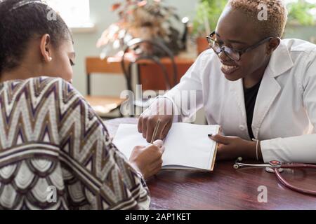 Patienten Mädchen mexikanischen Zeichen eine Behandlung mit einer schwarzen Frau Doktor junge Menschen von gemischten Rennen im Doktorbüro. Gemütliche Atmosphäre Lächeln p Stockfoto