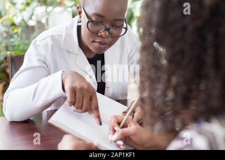 Patienten Mädchen mexikanischen Zeichen eine Behandlung mit einer schwarzen Frau Doktor junge Menschen von gemischten Rennen im Doktorbüro. Gemütliche Atmosphäre Lächeln p Stockfoto