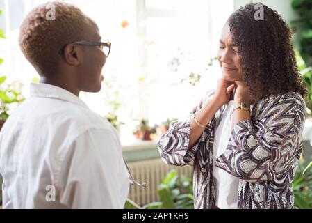 Mexikanische Patient klagt über Nackenschmerzen, afrikanische Frau Doktor, im Büro. Gemischten Rennen junge Menschen Stockfoto