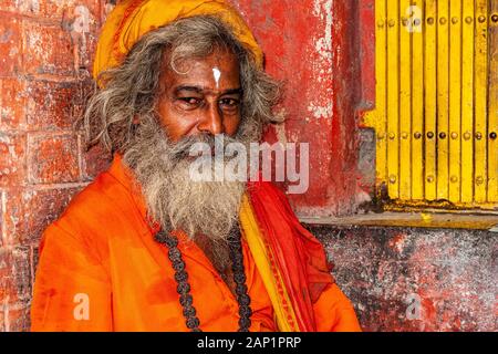 Ein sadhu, heiliger Mann, der orangefarbene Tücher trägt und vor einem kleinen Schrein sitzt Stockfoto