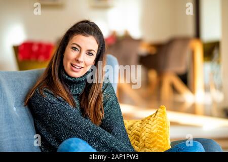 Schuß von attraktiven lächelnde Frau im Sessel sitzen und entspannt zu Hause. Stockfoto