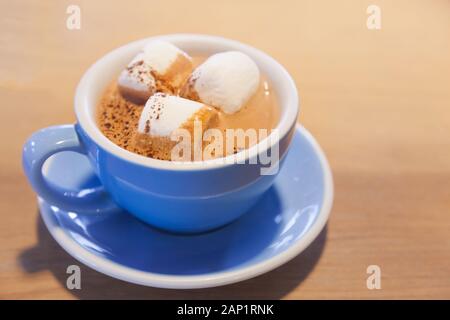 Trinken Sie heiße Schokolade mit Milch Latte Schaum gekrönt mit Marshmallow in blau Keramik Porzellan Schale auf holztisch Hintergrund. Entspannt Moment mit gesunden d Stockfoto
