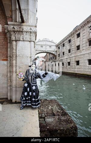 Eine Person in Karnevalsmaske, die sich mit der Brücke der Sichten im Hintergrund an eine Wand eines Gebäudes in Venedig Italien lehnt Stockfoto