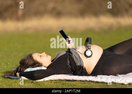 Schwangere Frau Festlegung auf dem Rücken auf dem Boden im Park mit Kopfhörern über ihren Bauch ein Kind in der Gebärmutter eine Chance, die Musik zu hören geben Stockfoto