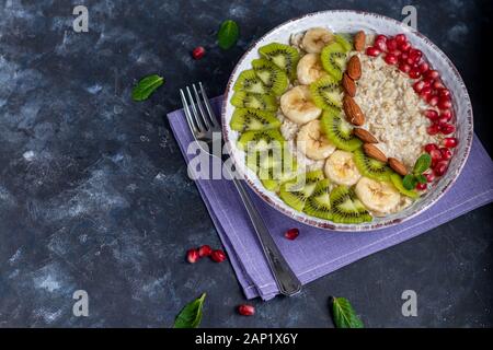 Frühstück bestehend aus Haferflocken, Nüsse und Früchte. Kiwi orange Granatapfel Mandeln Bananen ein Teller dekorieren. Das gesunde Essen, das auf einem dunklen Hintergrund. Kopieren Stockfoto