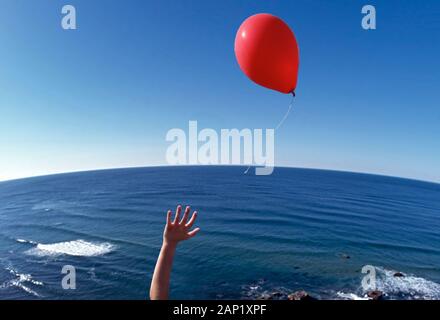 Ein Junge, der seinen roten Ballon über den Atlantik loslässt, gibt dem Ballon die Freiheit Stockfoto