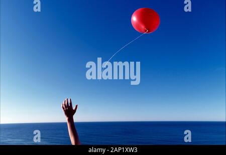 Ein Junge, der seinen roten Ballon über den Atlantik loslässt, gibt dem Ballon die Freiheit Stockfoto