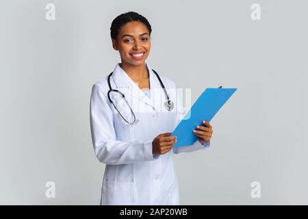 Jungen afro Ärztin im weißen Kittel mit Klemmbrett in der Hand Stockfoto