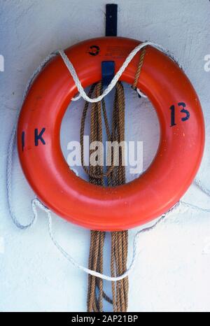 Orange Schwimmweste und Seil gegen eine weiße Wand Stockfoto