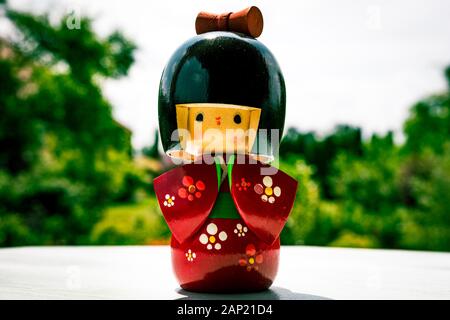 Japanische Kokeshi Puppe aus Holz, in traditionellem Kimono gekleidet, handbemalt in Rot und floralen Farben mit grünem Garten im Hintergrund Stockfoto