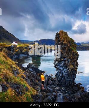 Touristen an einem felsigen Strand blicken auf ein kleines Haus in Arnarstapi, Island Stockfoto