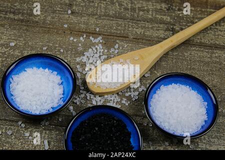 Nahaufnahme von drei isolierten blau Schüsseln mit verschiedenen Arten von Salz auf Holz Tisch mit Löffel (weiße Flocken, Körner, schwarz Hawaii Salz) Stockfoto