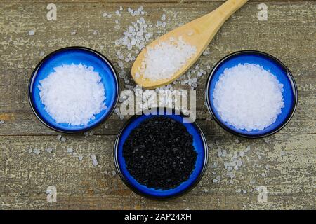 Nahaufnahme von drei isolierten blau Schüsseln mit verschiedenen Arten von Salz auf Holz Tisch mit Löffel (weiße Flocken, Körner, schwarz Hawaii Salz) Stockfoto