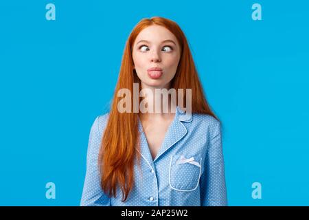 Witzig und albern. Redhead sorglos und begeisterte kaukasische Mädchen schielen, goofy Ausdruck, Zunge, ständigen blauen Hintergrund in Stockfoto