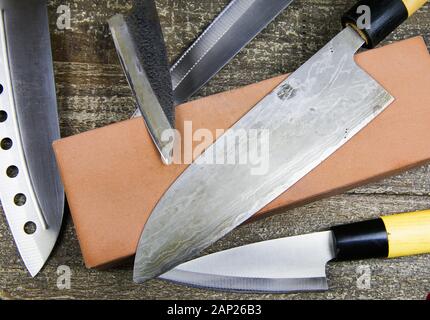 Schleifen Messer: Nahaufnahme von verschiedenen Metall japanische Küche Messer mit Schleifstein auf Holz Tisch Stockfoto
