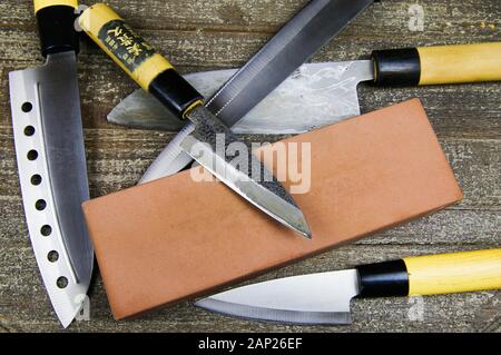 Schleifen Messer: Nahaufnahme von verschiedenen Metall japanische Küche Messer mit Schleifstein auf Holz Tisch Stockfoto