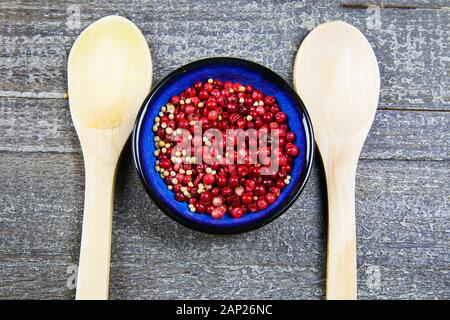 Detailansicht von oben auf Blau Schüssel mit rote Pfefferkörner, zwei Löffel auf Holz Tisch Stockfoto