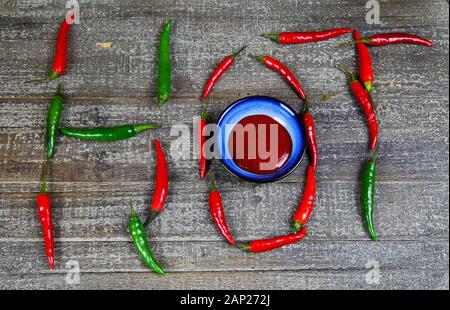 Hot scharfes Essen symbol Konzept: blaue Schale mit Chilisauce auf Holz Tabelle mit Grün rote Chilis bilden das Wort hot Stockfoto
