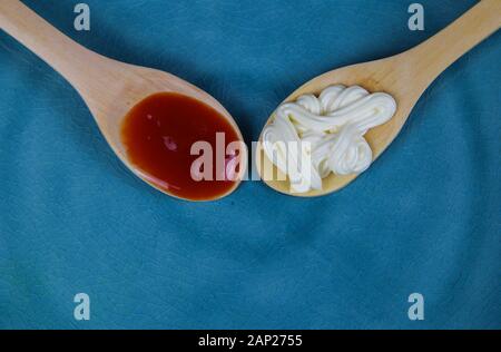 Nahaufnahme von zwei isolierten Holz Löffel mit Mayonnaise und Ketchup Rot auf Blau chine Platte Stockfoto