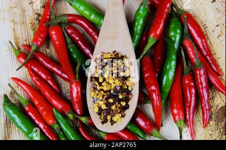 Hohen winkel Nahaufnahme auf isolierte Holz Löffel mit pikanten chili Flocken und rohe rote grüne Chilis auf natürliche braune Holz Platte Stockfoto