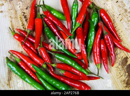 Hohen winkel Nahaufnahme auf isolierten Stapel raw rot grün Chilis auf natürliche braune Holz Platte Stockfoto