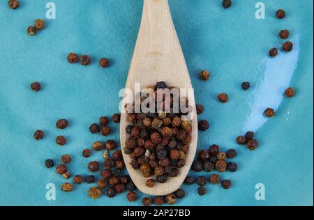 Nahaufnahme von isolierten Holz Löffel mit roten und schwarzen kambodschanischen kampot Pfefferkörner auf Blau alte verkratzte China Teller Stockfoto