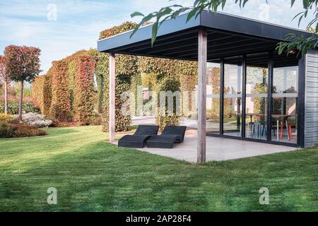Appeltern, Niederlande, 29. September 2017: Zwei schwarze Liegestühlen unter einem Überhang, um die Sonne zu genießen im schönen Herbst Garten Stockfoto