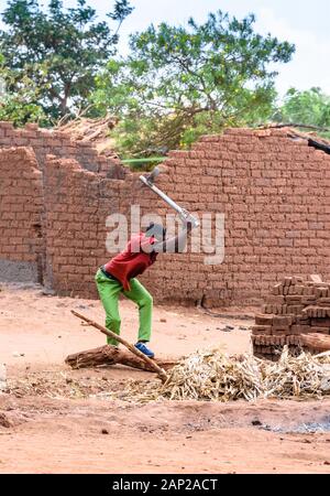 Ein malawischer Mann, der mit einer Axt Brennholz hackt, um in einem Dorf im Zentrum Malawis einen kleinen Ofen aus hausgemachten Backsteinen zu backen Stockfoto