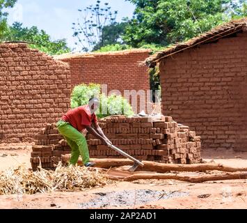 Ein malawischer Mann, der mit einer Axt Brennholz hackt, um in einem Dorf im Zentrum Malawis einen kleinen Ofen aus hausgemachten Backsteinen zu backen Stockfoto