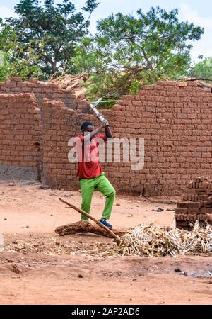 Ein malawischer Mann, der mit einer Axt Brennholz hackt, um in einem Dorf im Zentrum Malawis einen kleinen Ofen aus hausgemachten Backsteinen zu backen Stockfoto