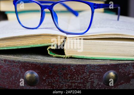 Blick auf alte open vergilbte Buch mit Blau Brille auf antiken Holztisch mit unscharfen Stapel Bücher Hintergrund Stockfoto